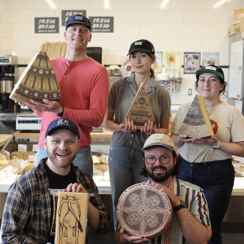 5 Cheesemongers holding up wheels of Swiss cheeses